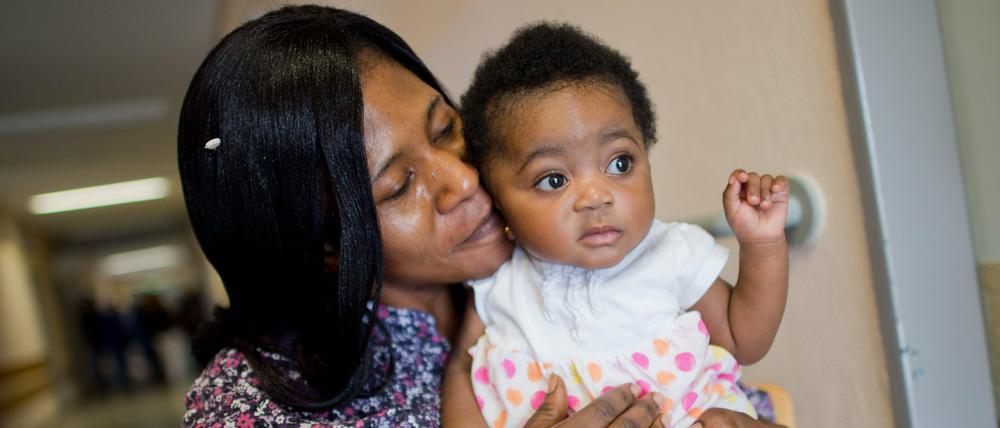 Die sechs Monate alte Angela Merkel Ade und ihre Mutter Ophelya Ade (26) sitzen am 13.08.2015 vor der Flüchtlingsunterkunft Oststadtkrankenhaus in Hannover (Niedersachsen). Ophelya Ade, ein Flüchtling aus Ghana, hat ihre Tochter nach der Bundeskanzlerin benannt, weil Merkel eine tolle Frau sei. In dem ehemaligen Krankenhaus sind 720 Flüchtlinge aus 33 Nationen untergebracht.
