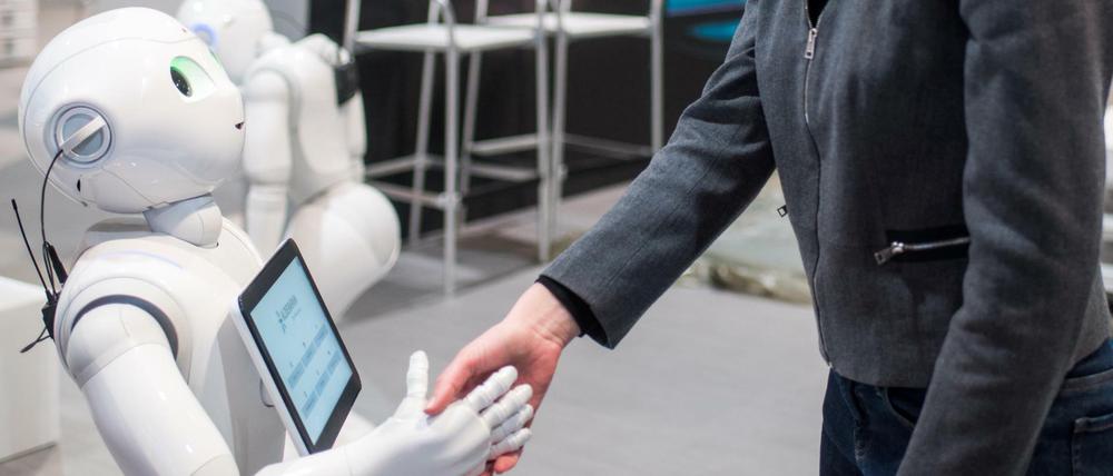 Die Kommunikationsmanagerin von Aldebaran, Aurora Chiquot, schüttelt auf dem Messegelände der CeBIT Hannover am Stand von Aldebaran dem humanoiden Roboter "Pepper" die Hand.