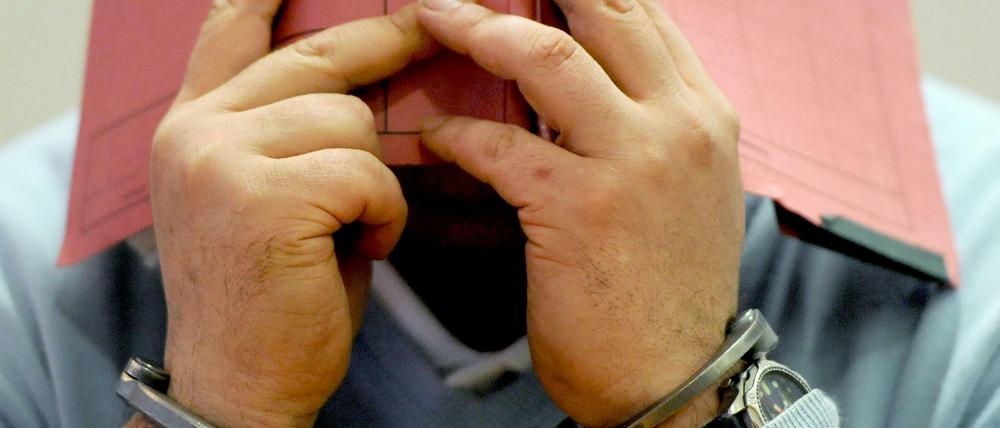 Der wegen mehrfachen Mordes und Mordversuchs an Patienten angeklagte, ehemalige Krankenpfleger Niels H. kommt am 09.12.2014 in Handschellen in den Gerichtssaal des Landgerichtes in Oldenburg (Niedersachsen) und hält sich wegen der anwesenden Medien einen Hefter vors Gesicht.