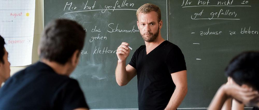 Ein Lehrer steht vor einigen Schülern an der Tafel und gestikuliert mit einem Kreidestück.