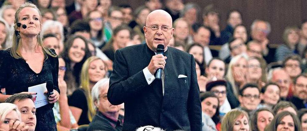 Ein Mann mit einem Mikrofon in der Hand steht inmitten von Studierenden, die in einem Hörsaal sitzen.