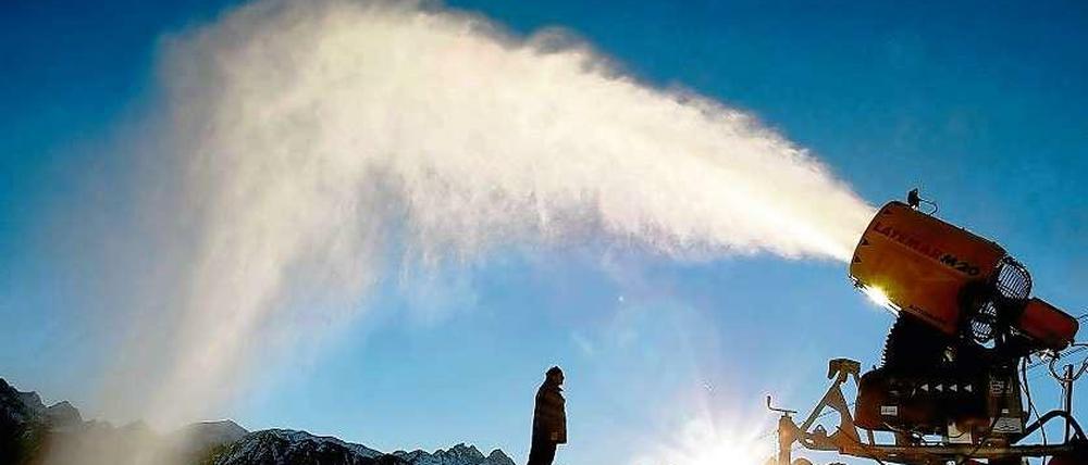 Eine Schneekanone schießt in hohem Bogen Schnee in den blauen Himmel.