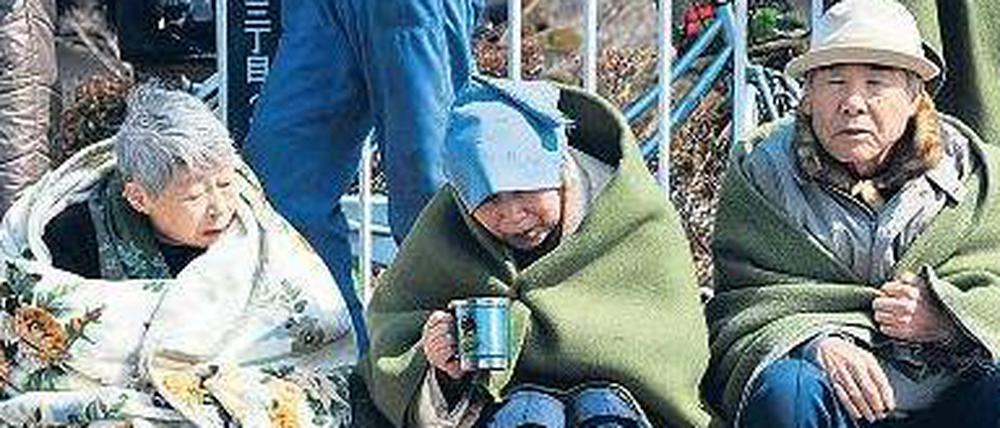 In Decken gehüllt warten Bewohner der zerstörten Stadt Ishinomaki auf Hilfe.