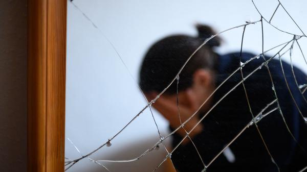 Eine Frau sitzt neben einem gesprungenen Spiegel auf einem Bett und hält ihren Kopf in den Händen (gestellte Szene). Die EU will Gewalt gegen Frauen den Kampf ansagen.