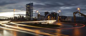 Die Scheinwerfer vorbeifahrender Autos ziehen an einer Brücke vor der Europäischen Zentralbank (EZB) Lichtspuren durch die Dunkelheit. 
