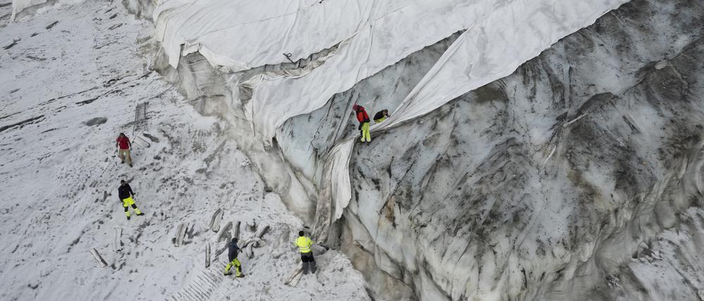 Blick auf den Corvatsch-Gletscher, waehrend Mitarbeiter der Bergbahnen Gletscher-Schutzvlies entfernen.  Glaziologen haben ihr Programm zur Vermessung des Gletschers eingestellt. Die Entscheidung wurde bereits im Jahr 2019 getroffen, doch der heiße Sommer 2022 hat zu «extremen Eisverlusten» und dem Ende des Programms geführt. Der bedeckte Teil des Gletschers wird im Winter als Skipiste genutzt. 