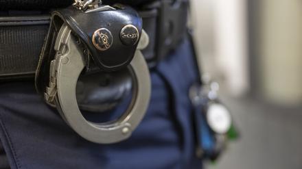 Eine Handschelle hängt am Gürtel eines Polizisten.