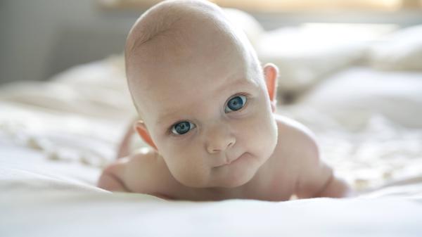 Ein Baby (Mädchen) liegt auf einem Bett und schaut in die Kamera.
