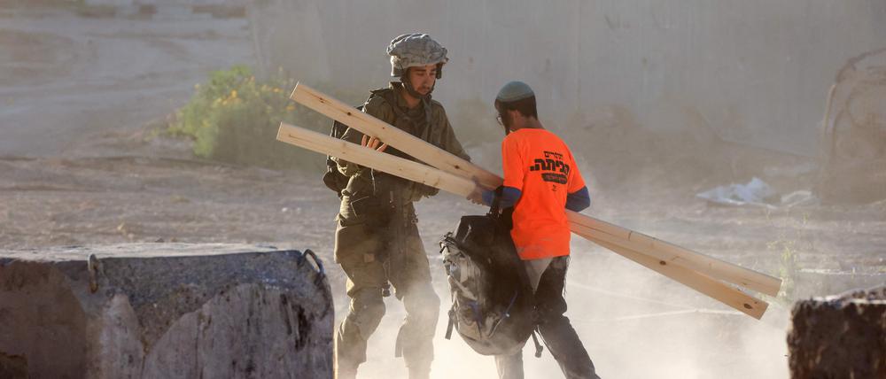 Ein israelischer Soldat fängt einen rechten Aktivisten ab, der Holz für den Bau eines Gebäudes in der Militärzone zwischen dem Zaun und der Mauer, die Israel vom Gazastreifen trennt, trägt. 