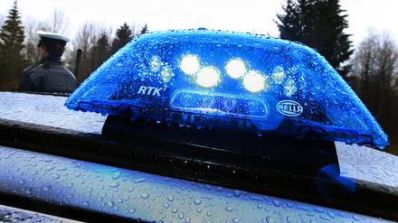 Ein Polizist steht im Regen vor einem Streifenwagen, dessen Blaulicht aktiviert ist. 