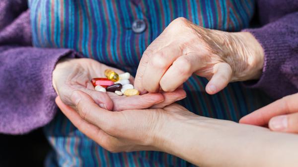 Eine ältere Frau mit bunten Pillen in der Hand.