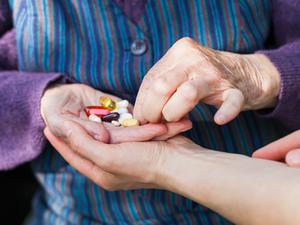 Eine ältere Frau mit bunten Pillen in der Hand.
