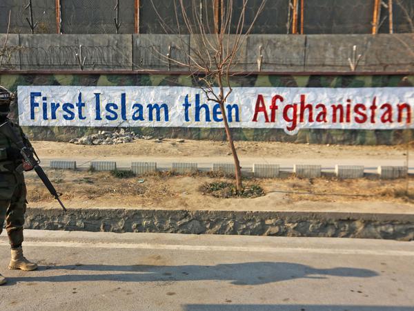 Ein Talib steht in einer Straße in Kabul vor einem Banner: „Erst Islam, dann Afghanistan“. 
