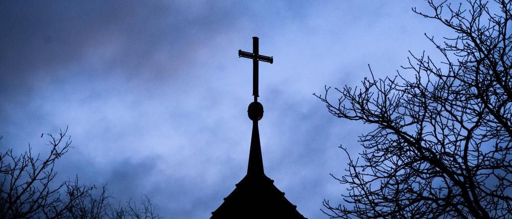 Dunkle Wolken ziehen über das Kreuz auf einer evangelischen Kirche in der Region Hannover hinweg.