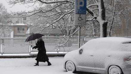 Eine Frau geht in Warschau bei Schneefall auf einem verschneiten Gehweg in Warschau und schützt sich dabei mit einem Regenschirm. 