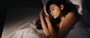 Eine Frau mit dunklen Haaren schläft nachts in einem Bett mit weißer Bettwäsche. 