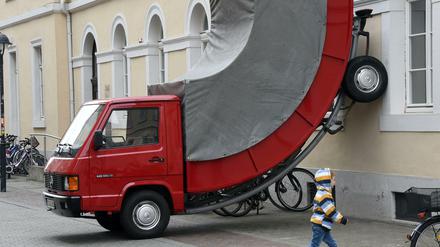 Der österreichische Künstler Erwin Wurm brachte das rote Fahrzeug an der Hauswand an. Da zwei Räder im Halteverbot standen, gab ein Polizist dem Wagen ein Knöllchen.