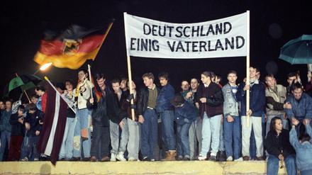Wendezeit: Berliner mit Fahne und Transparent "Deutschland Einig Vaterland" im Dezember 1989 auf der Mauer am Brandenburger Tor.