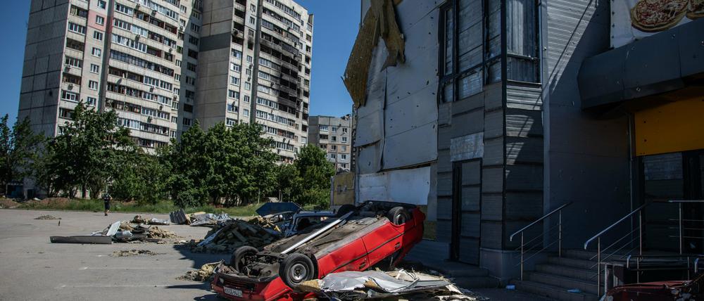 26.06.2022, Ukraine, Charkiw: Umgestürzte Autos und beschädigte Wohnhäuser in Saltiwka, einem großen Wohngebiet im nordöstlichen Charkiw.