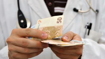 Ein Arzt hält Geldscheine in der Hand. 