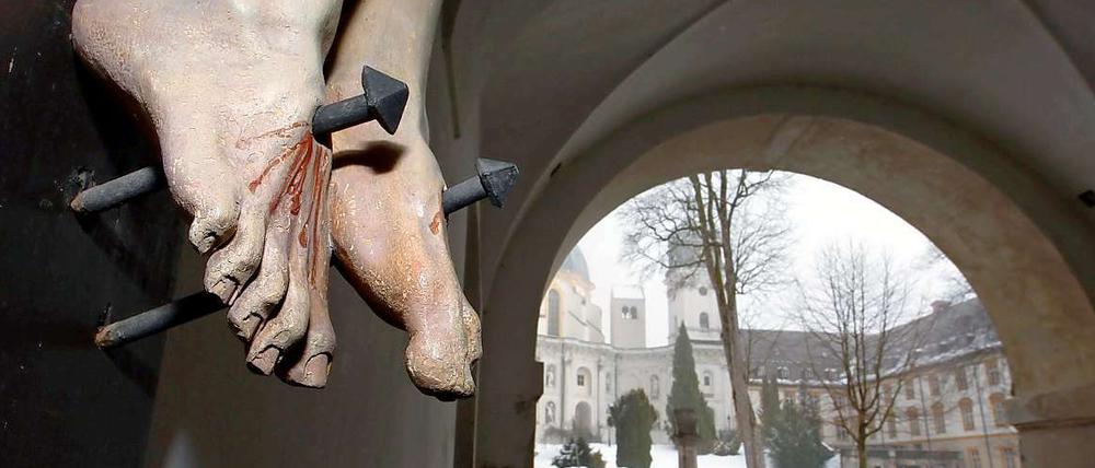 Die Füße einer gekreuzigten Christusfigur, aufgenommen am im Eingangsbereich des Klosters Ettal. Kinder wurden geschlagen und sexuell missbraucht. Die Vorfälle wurden vertuscht, Täter geschützt, Opfer alleingelassen. 