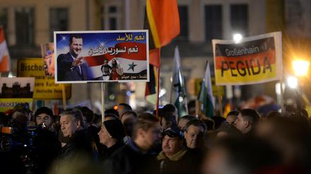 Pegida-Demonstration am 9. November in Dresden: Anhänger halten ein Plakat mit dem Antlitz des syrischen Präsidenten Baschar al-Assad hoch, auf dem in arabischer Schrift steht: "Wir sagen Ja zu Assad, Ja zu einem Syrien, das sicher ist".   