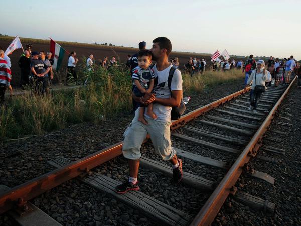 Flüchtlinge kommen am Mittwoch zu Fuß von Serbien nach Ungarn, nahe des Auffanglagers Rözke. Anhänger der rechten Jobbik-Partei protestieren am Rand.