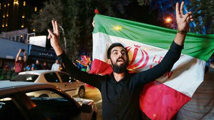 Im Iran wurde das Abkommen mit dem Westen über das Atomprogramm im Juli 2015 bejubelt. Ein Iraner zeigt in Teheran vor der Staatsflagge das Victory-Zeichen. 