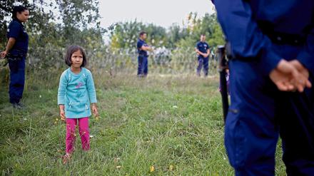 Ein Mädchen steht zwischen ungarischen Grenzbeamten, die es wegen illegalen Grenzübertritts festhalten.