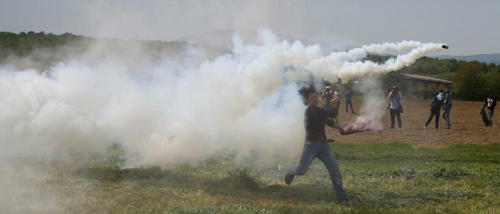 Flüchtlinge werfen Tränengasbomben zurück, die Polizisten am Grenzzaun zu Mazedonien abgefeuert haben.