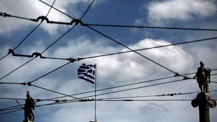 Athener Wirren. Die griechische Flagge, Athena (links) und Apollo durch die Oberleitungsdrähte einer Tram in der griechischen Hauptstadt gesehen. 