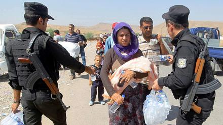 Bewaffnete Kräfte der kurdischen Peschmerga reichen jesidischen Flüchtlingen im Nordirak Wasserflaschen. 