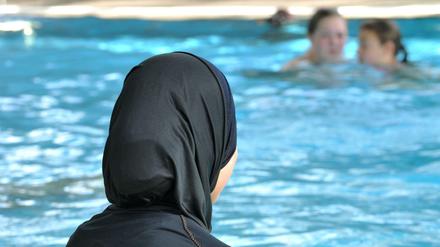 Eine muslimische Schülerin sitzt in einem Ganzkörper-Badeanzug am Rande des Schwimmbeckens. 