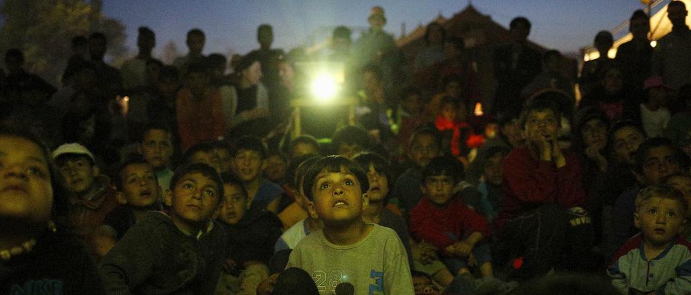 Kinder in Idomeni schauen einen Film auf einer Leinwand.