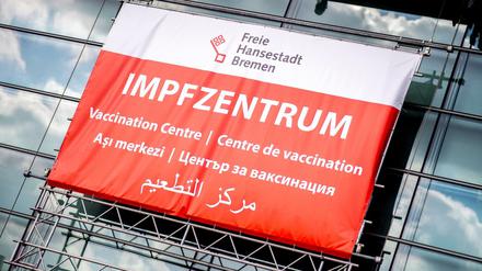 Ein Schild mit der Aufschrift ·Impfzentrum· in mehreren Sprachen hängt über dem Eingang des Impfzentrums in der Messehalle in Bremen.
