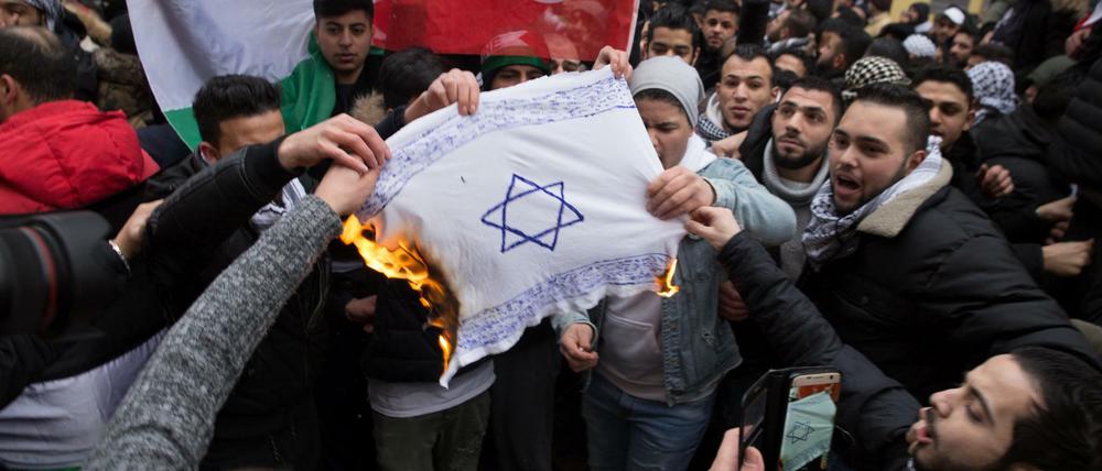 Teilnehmer einer Demonstration verbrennen eine selbstgemalte Fahne mit einem Davidstern in Berlin-Neukölln. 