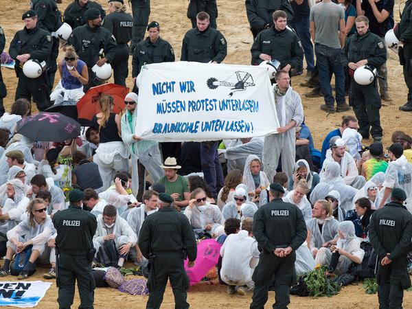 Polizisten haben im Tagebau Garzweiler in Erkelenz (Nordrhein-Westfalen) Braunkohle-Gegner eingekesselt, die ein Plakat mit der Aufschrift halten "Nicht wir müssen Protest unterlassen - Braunkohle unten lassen!".