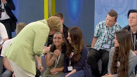 Bundeskanzlerin Angela Merkel (CDU) beugt sich am 15.07.2015 während der Veranstaltung in der von der Regierung gestarteten Gesprächsreihe "Gut leben in Deutschland" in Rostock zu einem Flüchtlingsmädchen palästinensischer Abstammung. Merkels Begegnung mit dem Kind hat in Sozialen Netzwerken zu Kritik geführt.