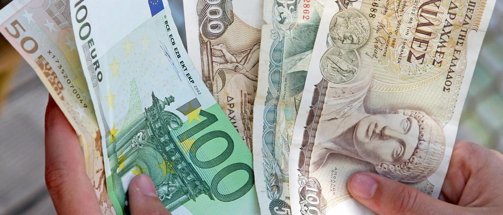 Ein Mann hält zwei Euro-Banknoten (Nennwert 50 und 100 Euro) und drei Drachme-Banknoten in den Händen (1000 und 500 Drachme). 