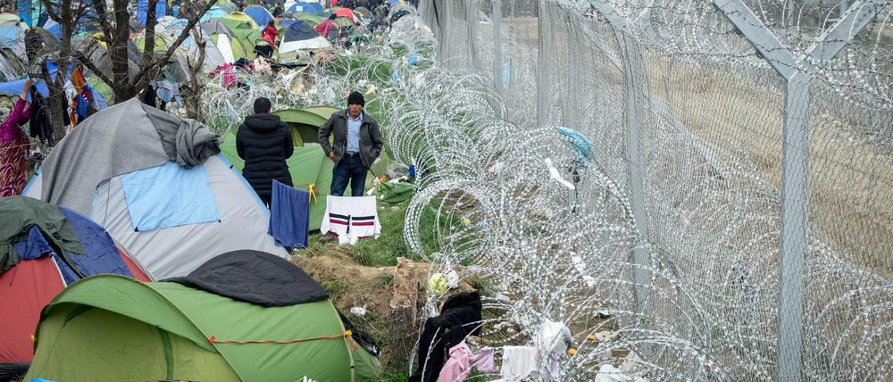 Flüchtlinge stehen am 07.03.2016 im Flüchtlingslager in Idomeni an der Grenze zwischen Griechenland und Mazedonien vor ihren Zelten am mit Stacheldraht gesicherten Grenzzaun. Nur noch wenige Flüchtlinge aus Syrien und dem Irak werden täglich über die Grenze gelassen. Foto: Kay Nietfeld/dpa +++(c) dpa - Bildfunk+++