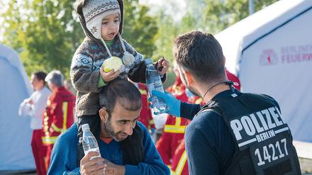 Ein Berliner Polizist verteilt Wasserflaschen an einen Vater aus Syrien und sein Kind, die zuvor mit weiteren Flüchtlingen am Bahnhof in Schönefeld (Brandenburg) angekommen waren.