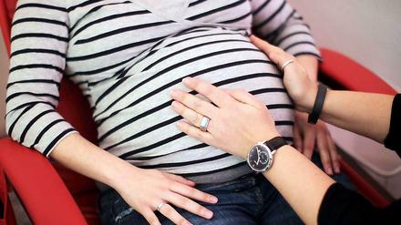 Eine Hebamme untersucht in einer Praxis eine schwangere Mutter. 