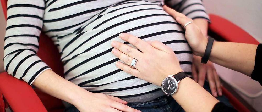 Eine Hebamme untersucht in einer Praxis eine schwangere Mutter. 