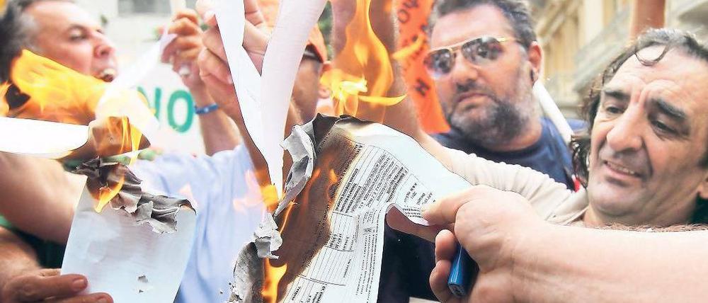 Weg damit. Empörte Staatsbedienstete verbrennen Steuerbescheide vor dem Finanzministerium in Athen. Sie wehren sich gegen eine Sondersteuer. Foto: Orestis Panagiotou/dpa
