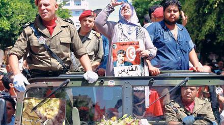 In Aufruhr. Zehntausende Tunesier gingen nach dem Mord an dem liberalen Oppositionspolitiker Mohammed Brahmi auf die Straße. Bei seiner Beerdigung hält seine Frau Mbarka ein Plakat von ihm in der Hand. Der Mordanschlag, hinter dem religiöse Extremisten vermutet werden, löste einen Generalstreik in Tunesien aus. Foto: Anis Mili/Reuters