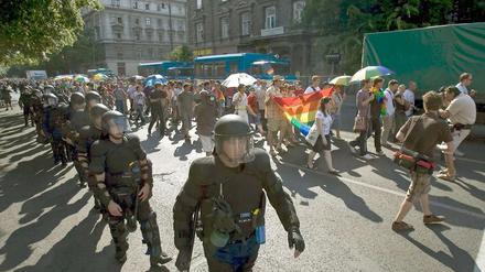 Polizisten in Kampfkleidung als Spalier neben ein paar hundert Demonstranten mit Regenbogenfahne