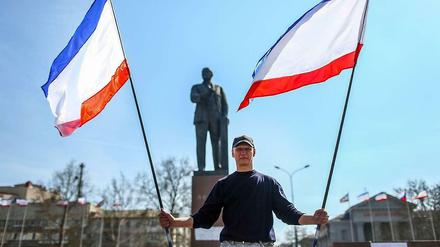 Ein Mann steht mit Fahnen der autonomen Republik Krim vor dem Lenin-Denkmal in Simferopol