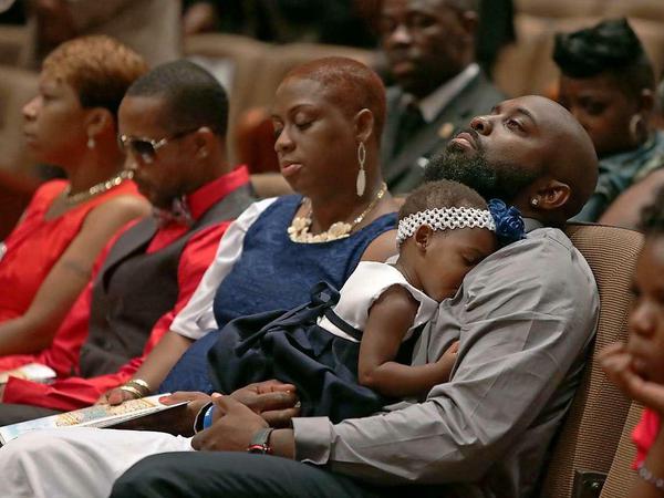 Der Vater von Michael Brown mit einem Baby auf dem Arm beim Trauergottesdienst für seinen Sohn. Neben ihm sitzt seine zweite Frau im blauen Kleid. Zwei Stühle weiter die Mutter von Michael Brown. 