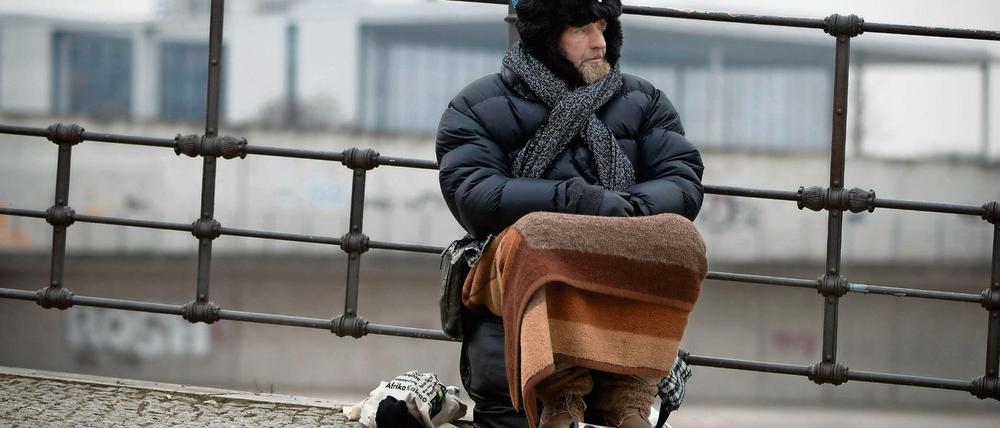 Udo, ein Obdachloser, sitzt im Winter in Berlin an der Spree im Regierungsviertel und bittet um Unterstützung.