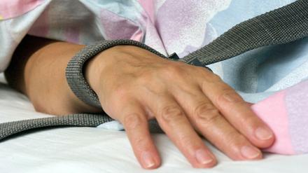 Eine Patientin in der Krankenpflege ist mit einem Textilband an der Hand festgebunden. 
